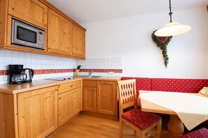 Ett kompakt kök med träskåp, en mikrovågsugn, en kaffebryggare och en röd, klädd bänk.
