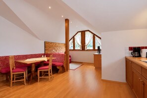 A dining area with a wooden table and chairs, a red patterned bench, and a kitchen with a coffee maker. - Holiday apartment in an Alpine setting (Achenkirch)