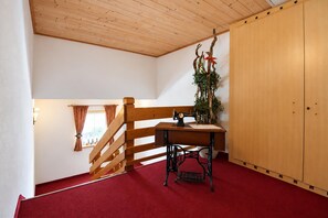 A room with a wooden staircase, a sewing machine on a table, a plant, and a wardrobe. - Holiday apartment in an Alpine setting (Achenkirch)