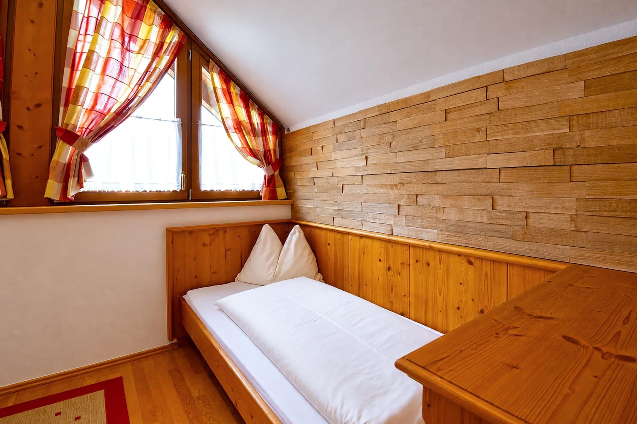 Una habitación pequeña con cama individual, paredes de madera y techo inclinado.