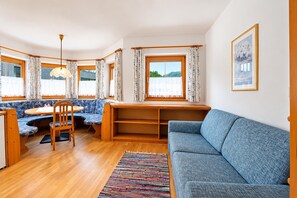 A cozy room with a wooden dining table, a blue sofa, and a window with curtains. - Modern holiday apartment near Lake Achensee (Achenkirch)