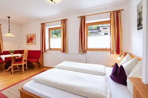 Una habitación de hotel con cama, zona de estar con mesa y dos ventanas con cortinas.