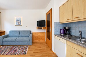 A compact living space with a sofa, a television on a shelf, a coffee maker, and a dishwasher. - Modern holiday apartment near Lake Achensee (Achenkirch)