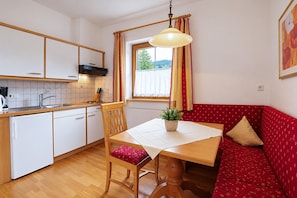A compact kitchen with white cabinets, a wooden dining table, and a red patterned sofa. - Modern holiday apartment near Lake Achensee (Achenkirch)