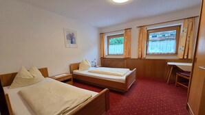 Et hotelværelse med to senge, et skrivebord, en stol, et natbord, en lampe og et vindue med gardiner.