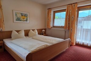 A hotel room with a large bed, a bedside table, a lamp, a window with curtains, and a painting on the wall.