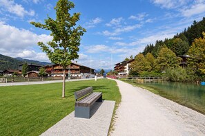 A riverside walkway with a bench, wooden buildings, and a mountain backdrop. - Modern holiday apartment near Lake Achensee (Achenkirch)