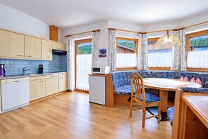 A compact kitchen with wooden cabinets, a built-in oven, and a dining area with a bench and table. - Modern holiday apartment near Lake Achensee (Achenkirch)