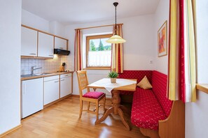 A compact kitchen with a dining area, a window with curtains, and a red sofa. - Modern holiday apartment near Lake Achensee (Achenkirch)