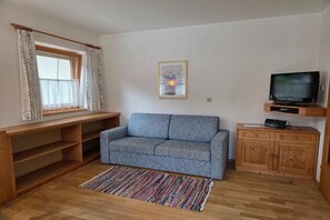 Una sala de estar con un sofá, una televisión, un mueble de madera y una ventana con cortinas.