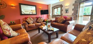 Ein Wohnzimmer mit Ledersofas, einem Couchtisch mit Snacks, einem Flachbildfernseher und einem großen Spiegel.