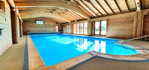 Ein großzügiger, überdachter Pool mit Holzwänden und hoher Decke.