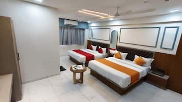 A hotel room with two beds, a small table, a ceiling fan, and a window with curtains.