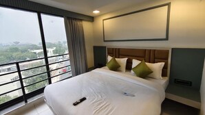 A hotel room with a large bed, a view through a window, and a mounted television. - HOTEL HILL VIEW (Ahmedabad)