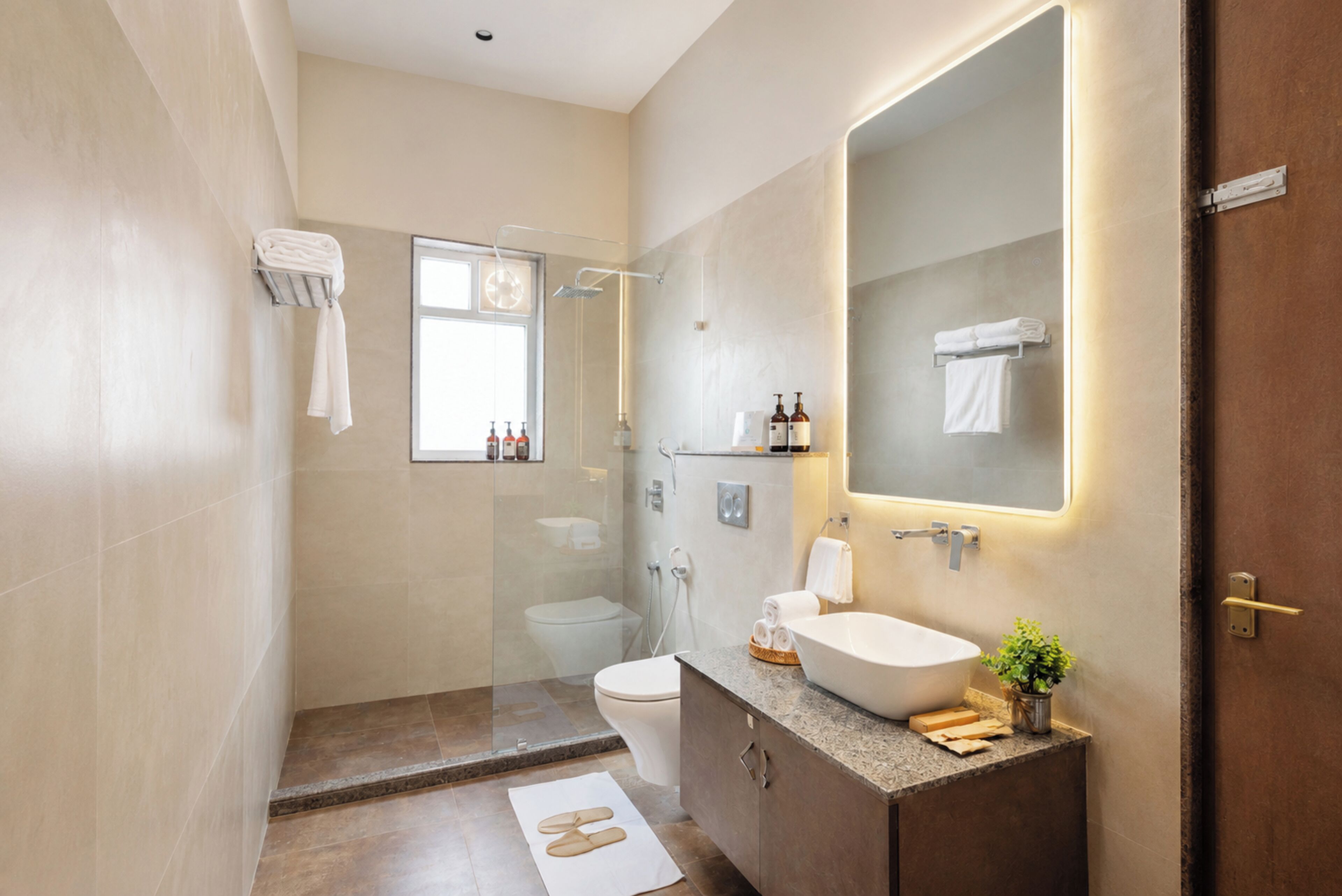 A modern bathroom with a glass-enclosed shower, a toilet, a sink with a large mirror, and neatly folded towels on a rack.