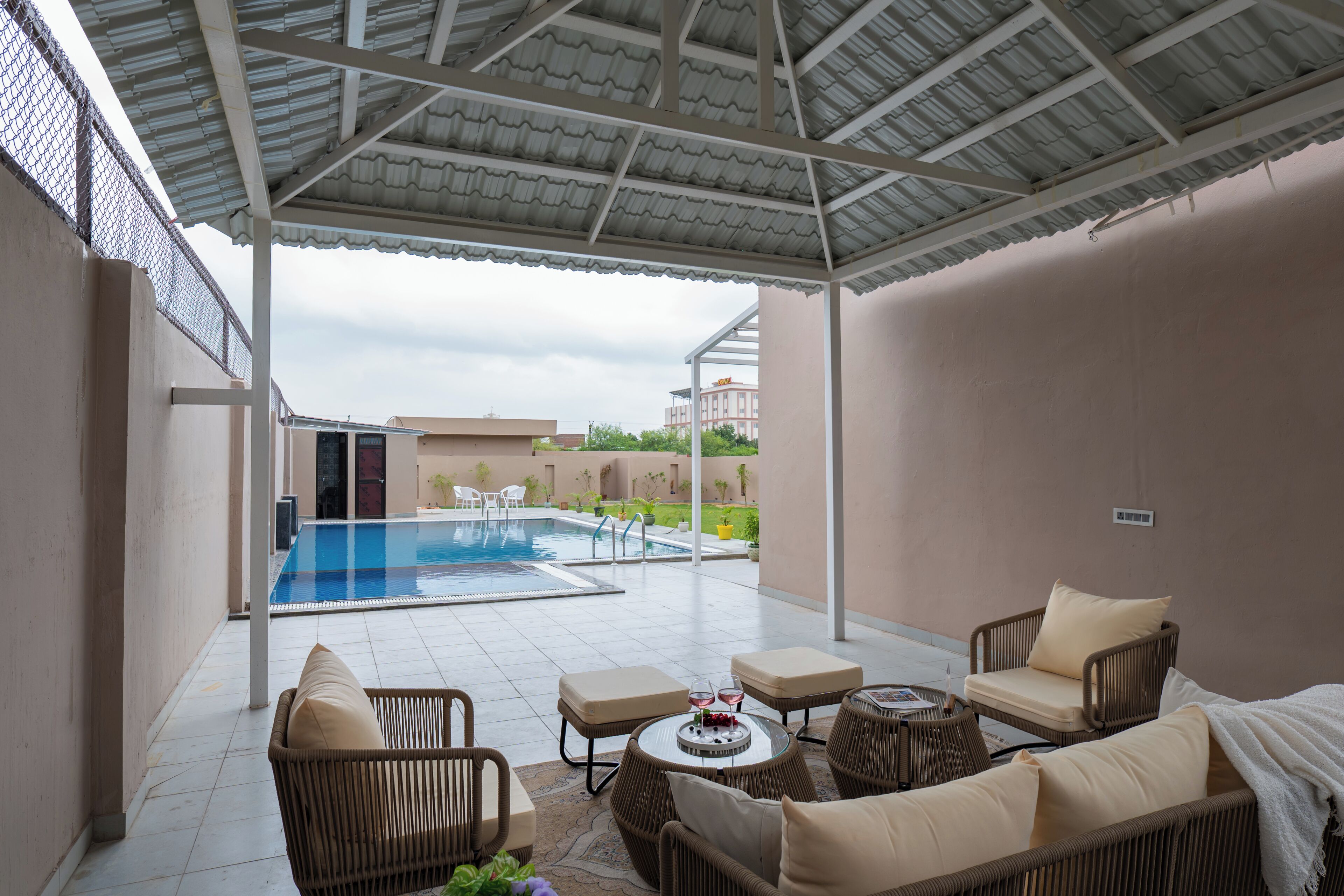 A covered outdoor area with a pool, seating, and a view of buildings in the background.