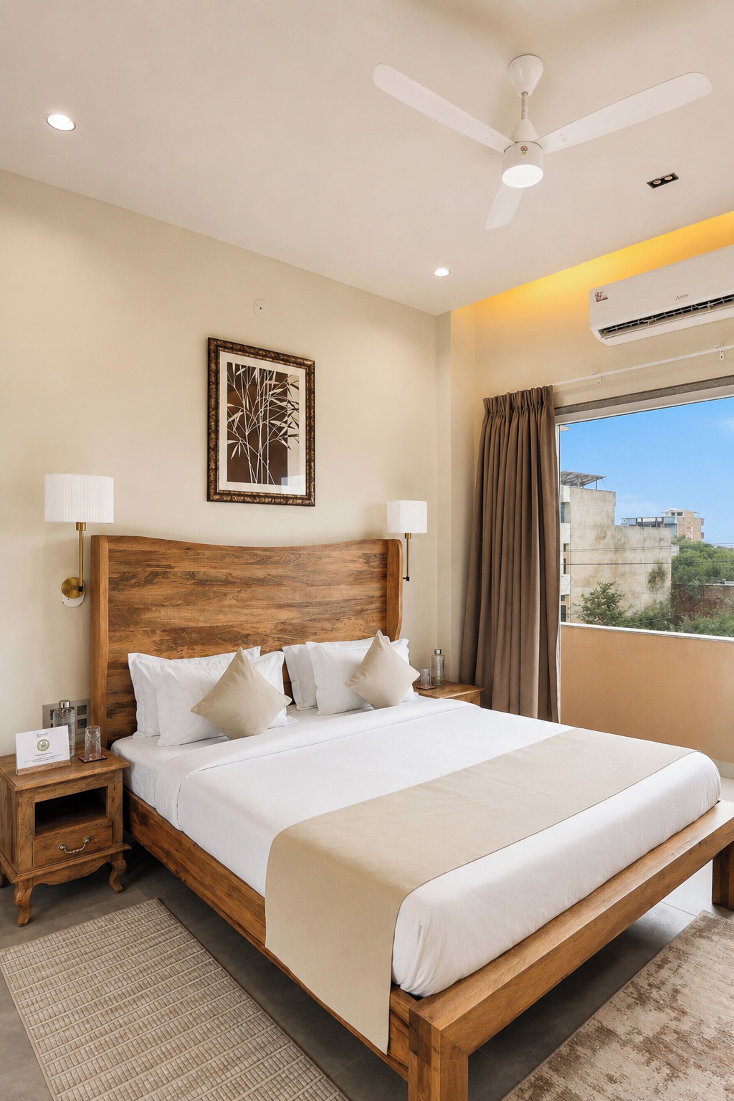 A hotel room with a large bed, wooden headboard, two bedside tables, a ceiling fan, and a window with curtains.