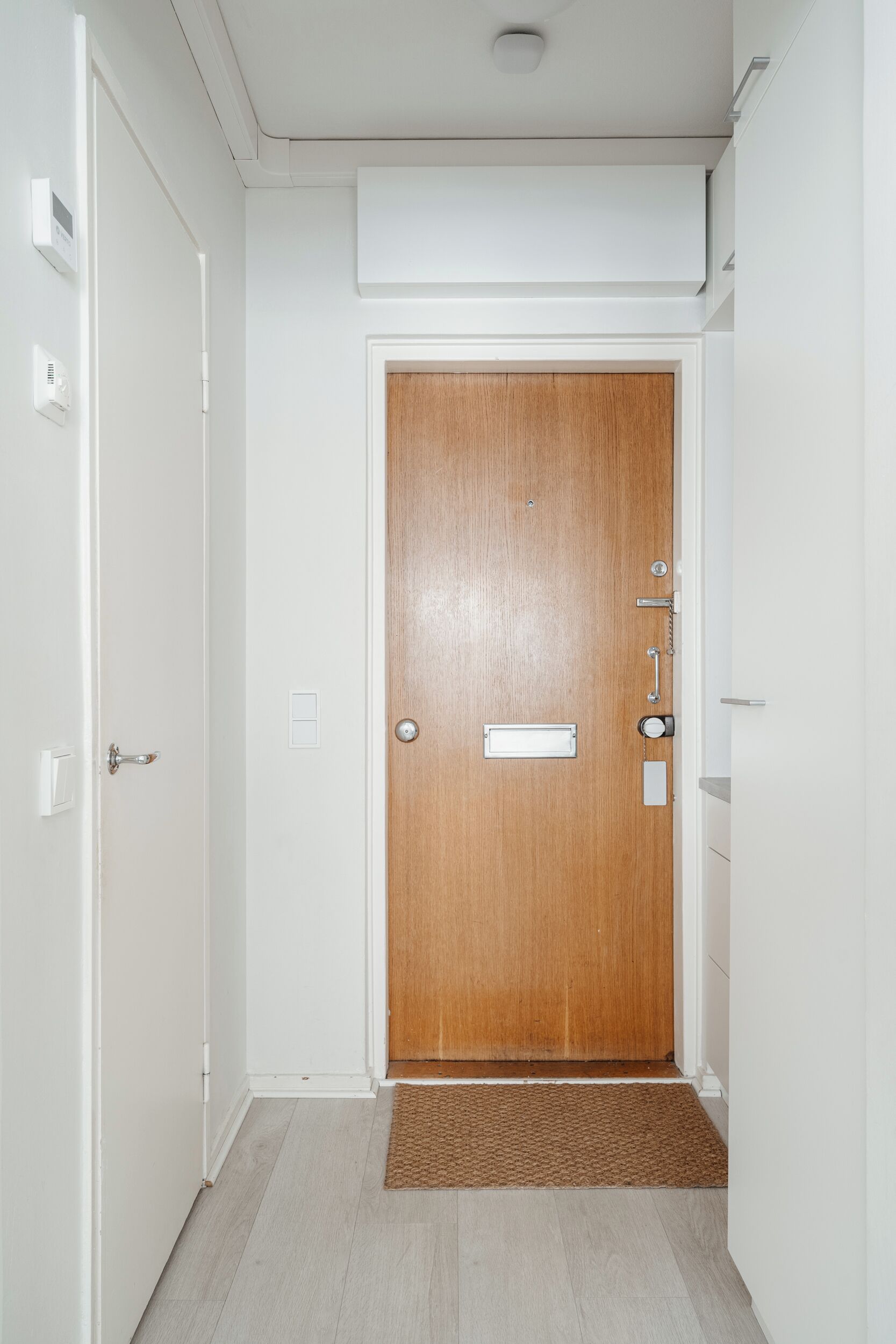 A hallway with a wooden door, a doormat, and a light switch on the wall.