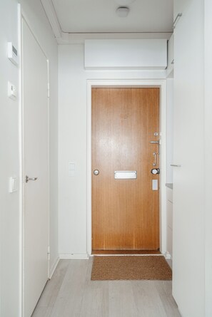 A hallway with a wooden door, a doormat, and a light switch on the wall. - Cozy Punavuori Studio with 600Mbit WiFi (Helsinki)