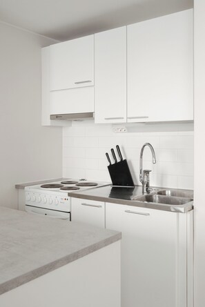 A modern kitchen with white cabinets, a stainless steel sink, and a gas stove. - Cozy Punavuori Studio with 600Mbit WiFi (Helsinki)
