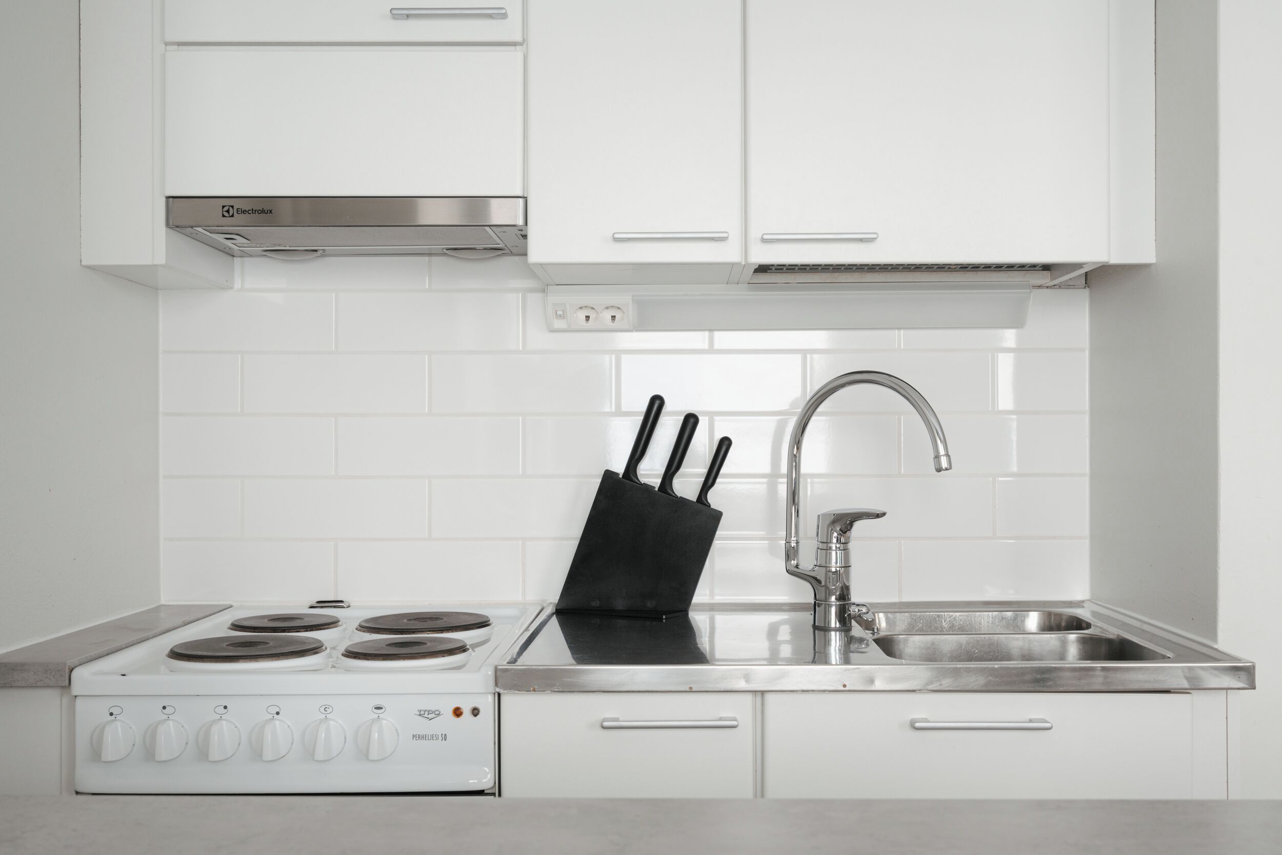 A modern kitchen with white cabinets, a stainless steel range, a sink, and a knife block.