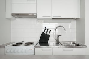 A modern kitchen with white cabinets, a stainless steel range, a sink, and a knife block. - Cozy Punavuori Studio with 600Mbit WiFi (Helsinki)
