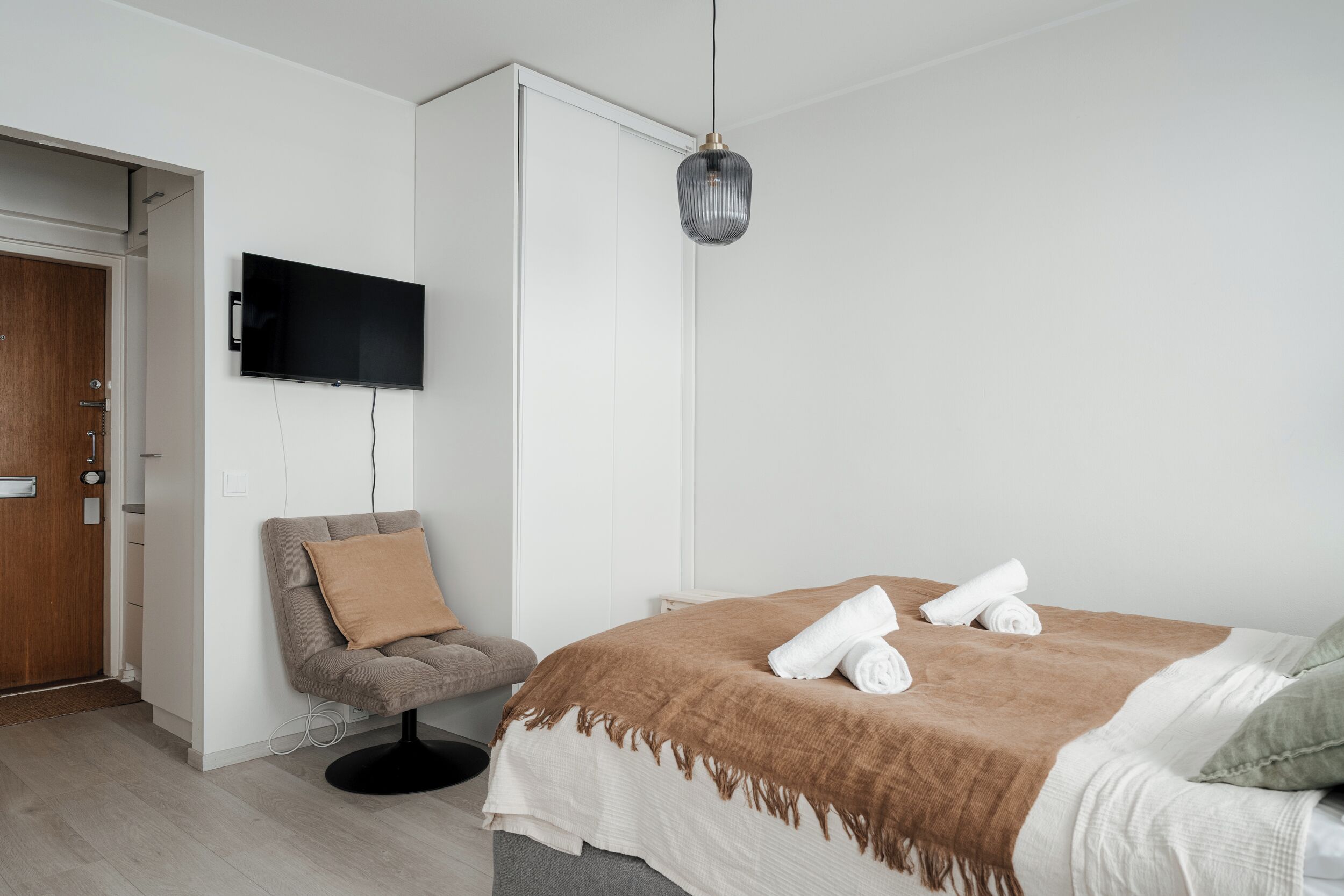A modern bedroom with a bed, a chair, a television, and a door.
