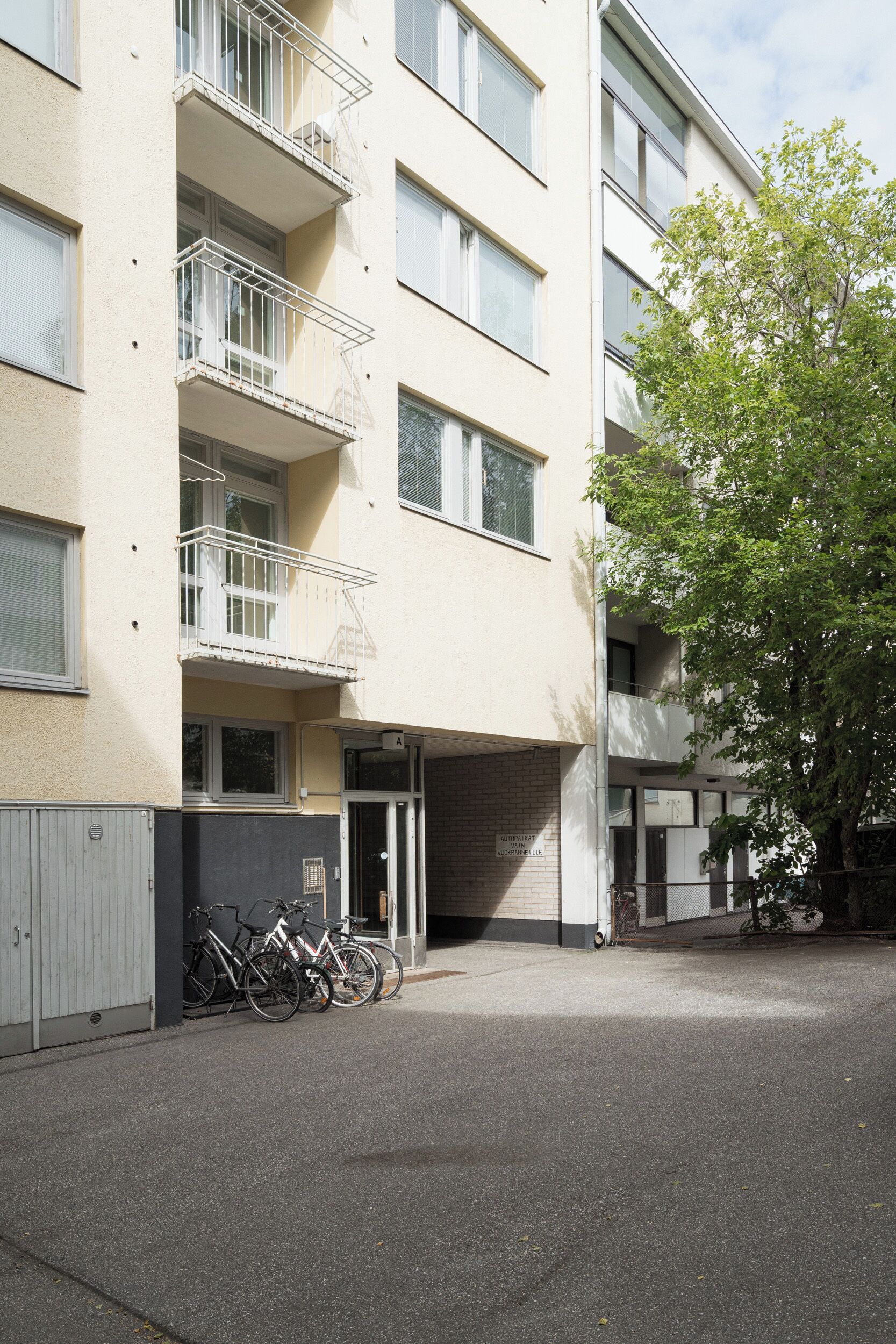 A multi-story residential building with balconies, a gated entrance, and bicycles parked outside.
