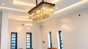 A spacious room with a modern chandelier, two upholstered chairs, a sofa, and large windows. - Seychelles Bella House (Mahé)
