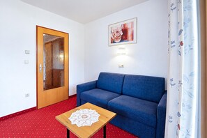 Ein Zimmer mit einem blauen Sofa, einem Holztisch mit einer Tischdecke, einer Tür mit Frostglas und einer Wandleuchte.