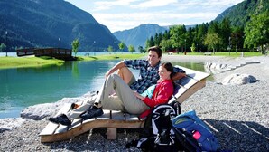 Un couple se détend sur un banc en bois au bord d’un lac, avec des montagnes en arrière-plan.