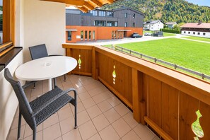 A balcony with a table and chairs, overlooking a grassy area and buildings. - Apartment near the lake (Achenkirch)