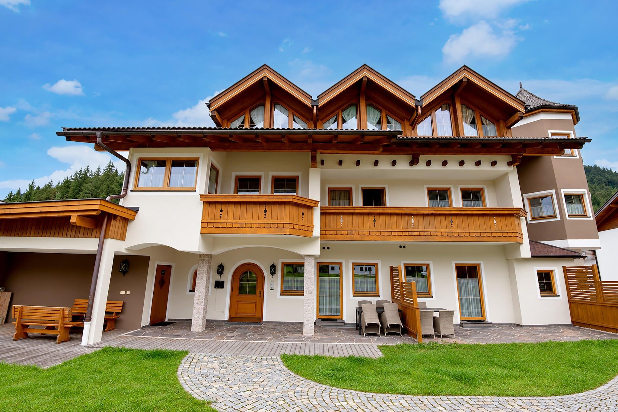 A two-story house with a balcony, a stone pathway, and a grassy lawn.