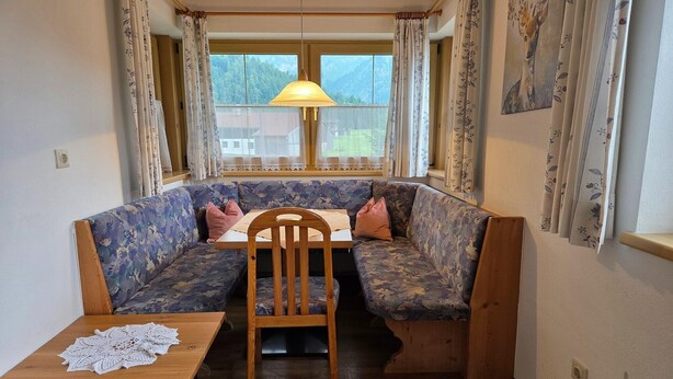 Un coin salon confortable avec un banc et une table, une lampe et une fenêtre avec des rideaux.