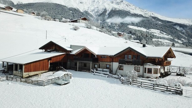 A chalet-style building with a snow-covered roof, surrounded by a wooden fence, set against a backdrop of snow-covered mountains. - Panoramic View Suite on the Kaunergrat (Kaunerberg)