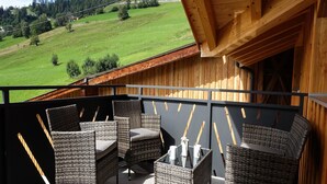 A balcony with wicker furniture, a view of a green landscape, and a wooden building structure. - Panoramic View Suite on the Kaunergrat (Kaunerberg)