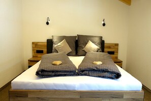 Ein ordentlich bezogenes Bett mit einer weißen Matratze und dunklem, gemustertem Bettzeug, begleitet von Holz-Kopfteilen und Nachttischen.