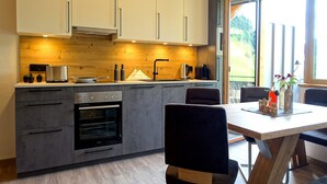 A modern kitchen with built-in appliances, a dining area with a wooden table and chairs, and a large window providing a view of the outdoors. - Panoramic View Suite on the Kaunergrat (Kaunerberg)