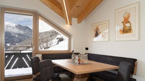 A modern interior with a wooden table and black chairs, large windows with a snowy mountain view, and two framed artworks on the wall. - Panoramic View Suite on the Kaunergrat (Kaunerberg)