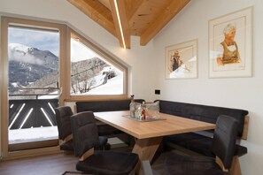 Ein modernes Interieur mit einem Holztisch, schwarzen Stühlen, großen Fenstern mit Blick auf einen verschneiten Berg und zwei gerahmten Kunstwerken an der Wand.
