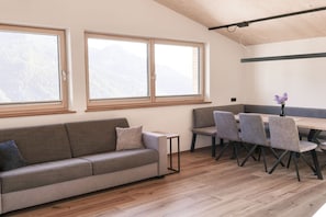 Ein modernes Wohnzimmer mit Sofa, Esstisch und Stühlen, großen Fenstern mit Bergblick und Holzböden.