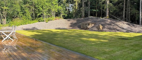 Une terrasse en bois, une pelouse verdoyante et un muret en pierre.