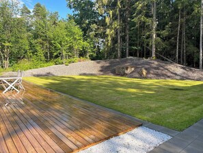 Eine Holzterrasse mit Rasenfläche und einer Steinmauer.