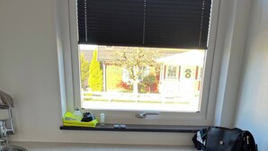 Ett tvättrum med två vita tvättmaskiner som har frontmatning, ett fönster med persienner, ett handfat och en hylla med diverse föremål.
