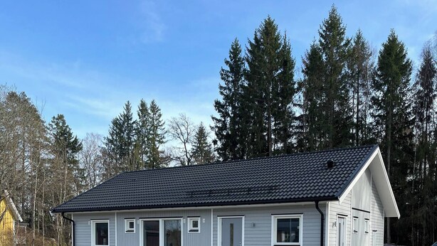 Ett envåningshus med ett mörkt tak, vit fasadbeklädnad och ett garage.