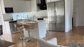 Ett modernt kök med vita skåp, ett kylskåp i rostfritt stål och en matplats med en vit soffa och två barstolar.