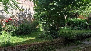 Un jardín con muro de ladrillo, diversas plantas y una terraza de madera.