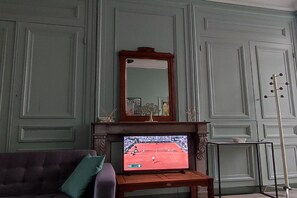 Ein Zimmer mit Fernseher, der ein Tennismatch zeigt, Kamin und Spiegel an der Wand.