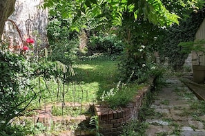 Un jardín con muro de ladrillo, distintas plantas y un camino de piedra.