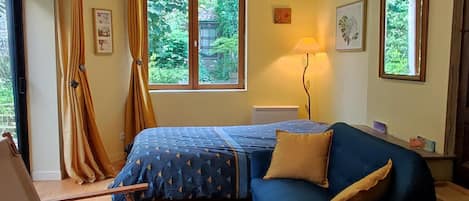 Ein Schlafzimmer mit Bett, Sessel, Lampe und einem Fenster mit Vorhängen.